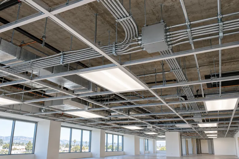 An open commercial ceiling with conduit runs, cable bundles and LED troffers during a tenant improvement